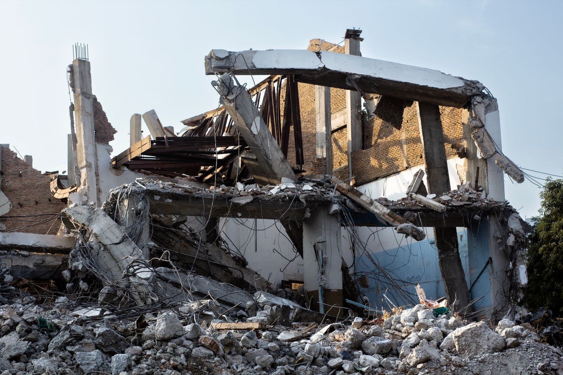 A partly demolished concrete and brick building with slabs, columns and bent steel hanging above a pile of rubble.