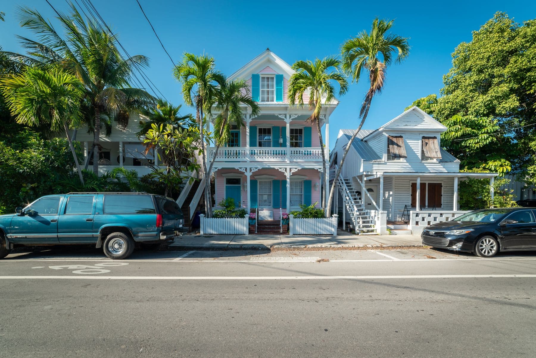 Two painted wooden houses with white porches and palm trees on a sunny street in Key West, Florida.