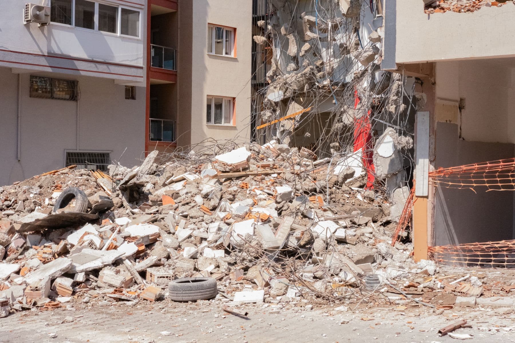 A pile of broken concrete, brick and wire beside an apartment building where one section has been demolished.