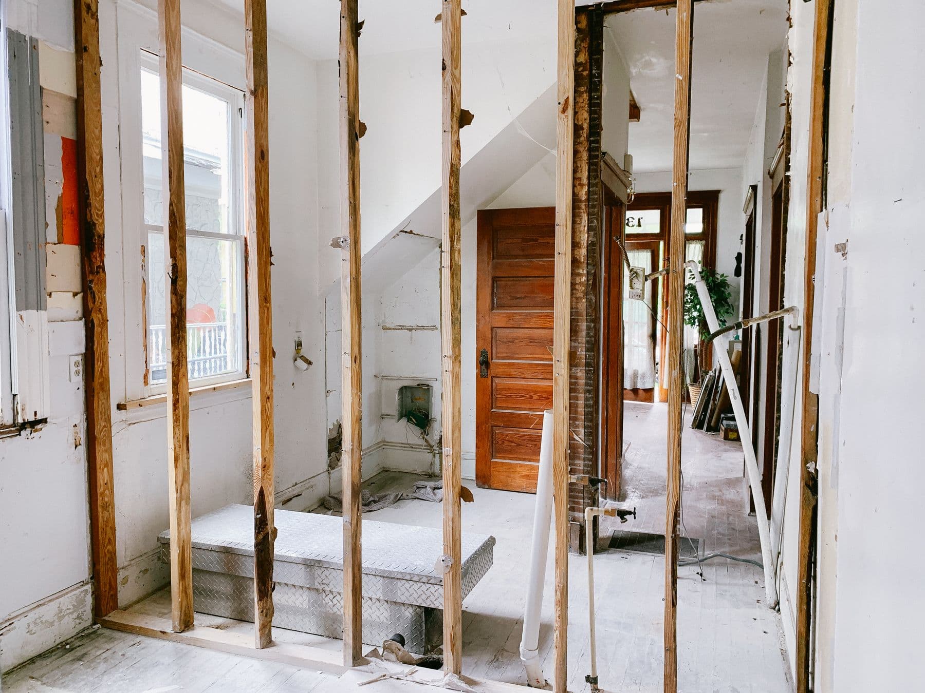 The inside of an older house with the walls stripped back to bare studs, a wood door and pipes visible beyond.