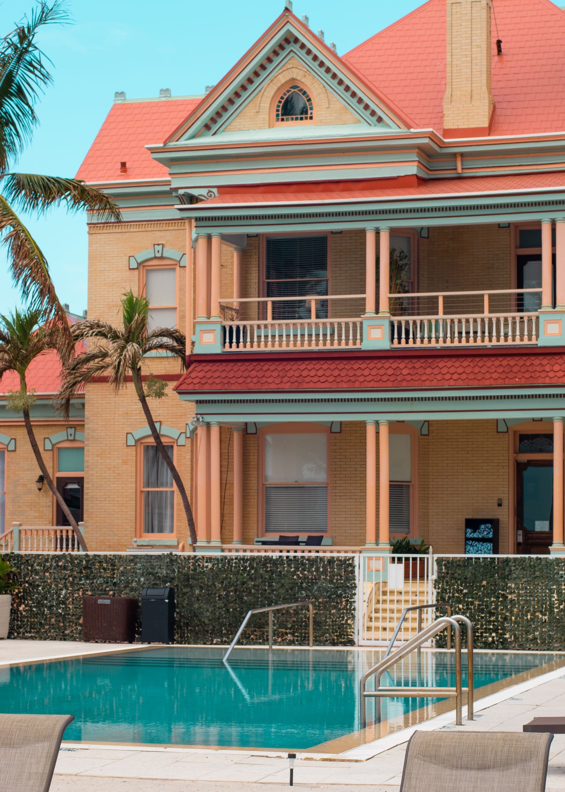 A swimming pool in front of a large Victorian-style building with a red roof, balconies and palm trees in Key West.