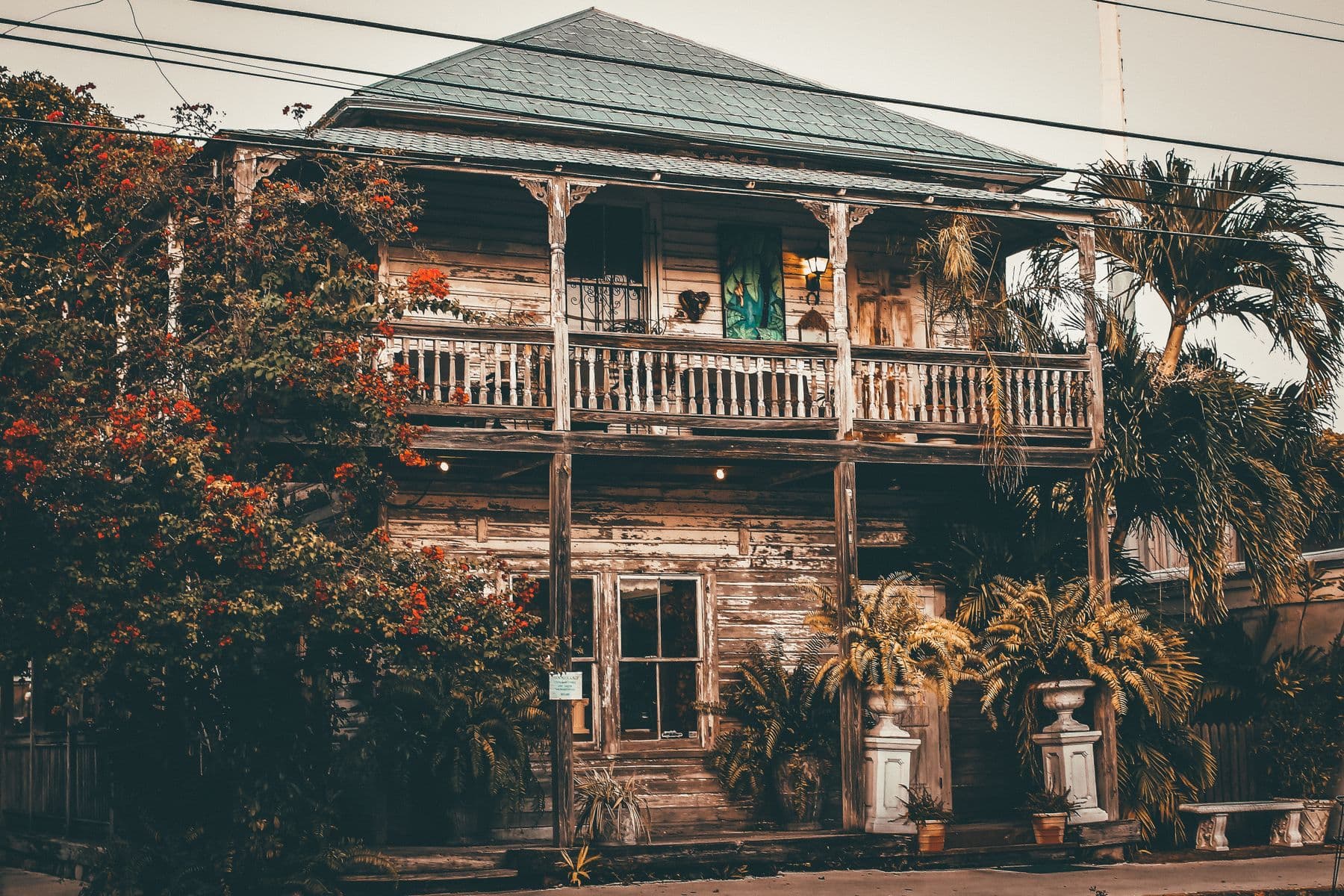 A two-story weathered wooden house with an upper porch, surrounded by palms and bougainvillea in Key West.